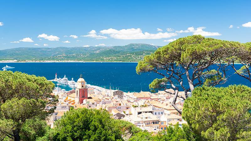 View over marina at St Tropez with a superyacht charter out at sea.