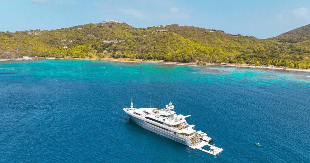 Motor Yacht Loon anchored off the bay of Mustique private island with clear blue coastline and lush vegetation